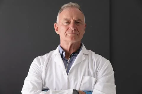 Portrait of caucasian senior male doctor wearing white coat standing with arms Stock Photos