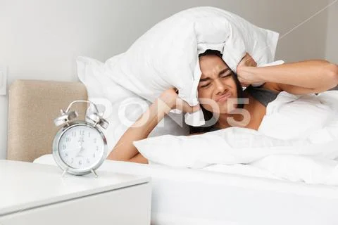 Portrait of caucasian upset woman shutting ears with pillow due to ringing al Stock Photos