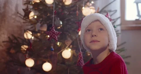 Portrait of cheerful boy in red hat looking above waiting santa claus present by Stock Footage 149680133