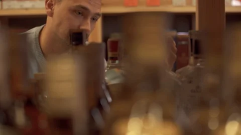 Portrait of cheerful man is taking gin bottle from the store shelf. Customer is Stock Footage 99385738