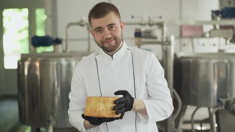 Portrait of a cheesemaker worker holding cheese in his hands and looking at the 库存影片 175323809