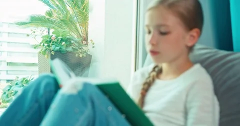 Portrait child reading book and laughing. Girl sitting on the floor near wind Stock Footage