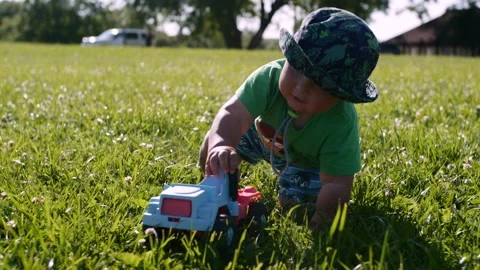 Portrait of a chubby kid in a panama hat playing with a car on the green grass. Stock Footage 146777841