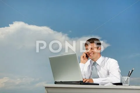Portrait of confident businessman calling by mobile and typing on the laptop Stock Photos