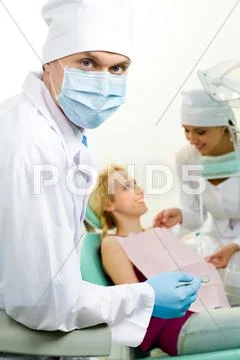 Portrait of confident doctor in sterile mask on background of his assistant help Stock Photos