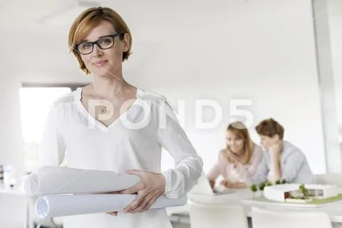 Portrait confident female architect holding blueprints in conference room Stock Photos