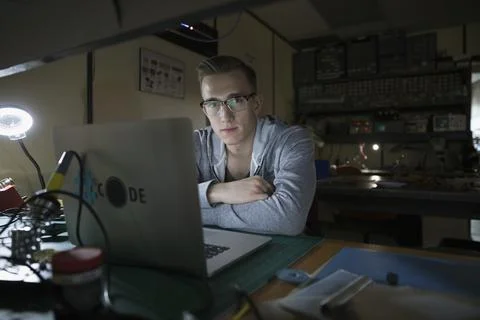 Portrait confident male computer programmer working at laptop in dark workshop 스톡 사진
