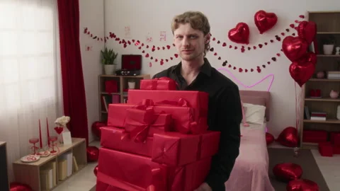 Portrait of Confident Young Man with Stack of Gift Boxes Wrapped in Red Paper Stock Footage 326632323