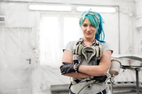 Portrait confident young woman with blue hair with paint gun in auto body shop Stock Photos