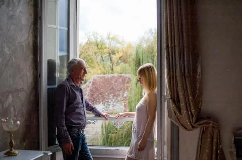 Portrait of Couple with Age Difference Standing near Opened Window inside the Stock Photos