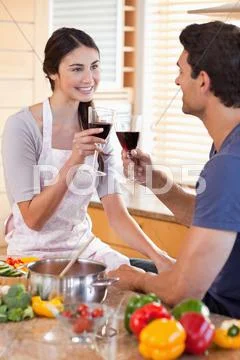 Portrait of a couple having a glass of wine while cooking Stock Photos