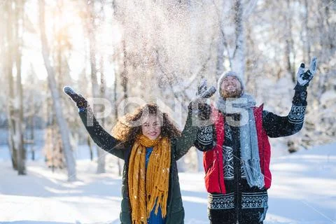 Portrait of couple standing outdoors in snow in winter forest, throwing snow. Stock Photos