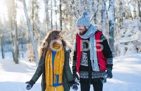 Portrait of couple walking outdoors in snow in winter forest, talking. Stock-Fotos