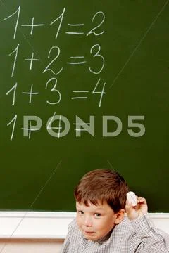 Portrait of curious schoolchild standing at blackboard with written sums on it a Stock Photos
