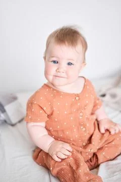 Portrait of a cute 9 months old baby girl seating on a bed. Stock Photos