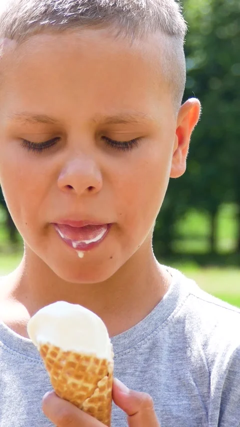 Portrait of cute 9-year-old boy in green park in summer eating cold ice cream Stock Footage 312145059
