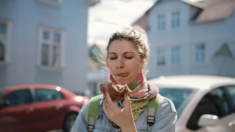 Portrait of cute attractive woman standing on street and eating the baked bun Stock Footage