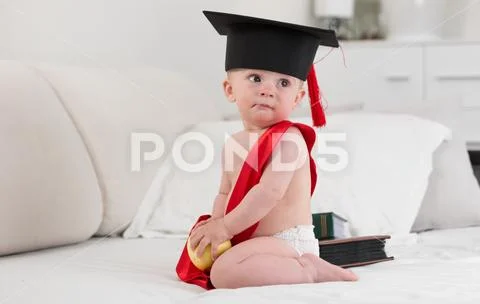 Portrait of cute baby boy in mortarboard hat sitting on bed at bedroom Stock Photos