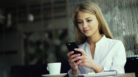 Portrait of a cute blonde female read something on her smart phone while sitting Stock Footage
