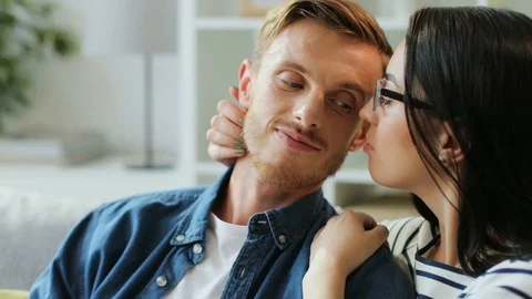 Portrait of cute couple sitting on the sofa, looking to each other, hugging and Stock Footage 79994124