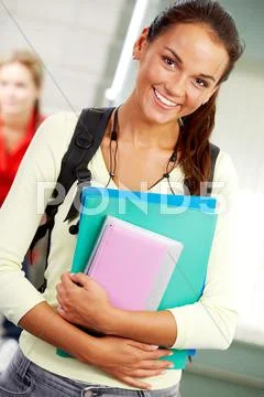 Portrait of cute girl with textbook in hands looking at camera in college Stock Photos