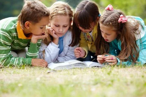 Portrait of cute kids reading book in natural environment together Stock Photos
