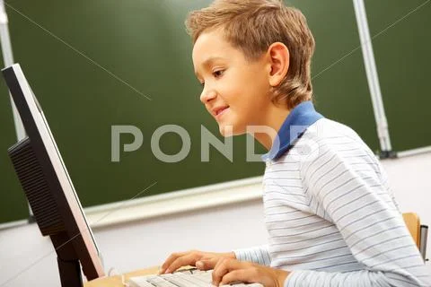 Portrait of cute lad typing on computer board in classroom Stock Photos