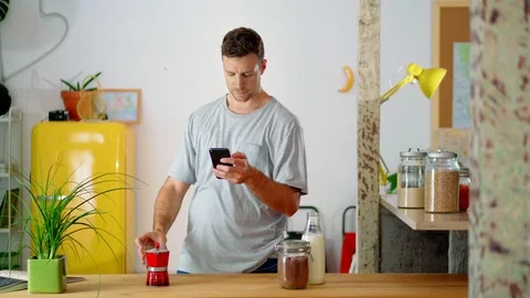 Portrait of cute morning guy drinking coffee near kitchen table and using Stock Footage 114915670
