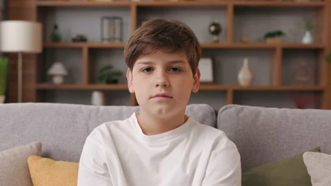 Portrait of cute young boy looking at camera sitting on a coach. Sad teenager 스톡 동영상 213282697