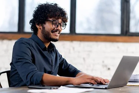 Portrait of dark-haired man using laptop in home office. Curly male entrepreneur Stock Photos