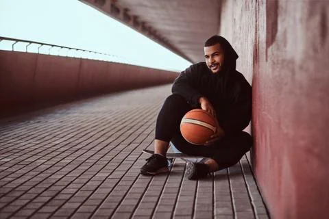 Portrait of a dark-skinned guy dressed in a black hoodie and sports shorts holds 写真素材