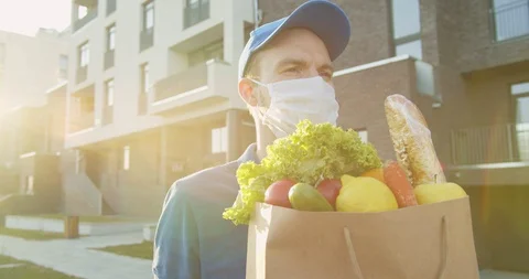 Portrait of delivery man wearing cap and medical mask carrying packet with fresh Stock Footage 129558089