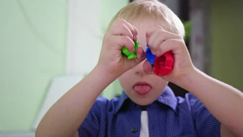 Portrait of disabled boy, child with Down syndrome shows tongue while playing at Stock Footage 139876512