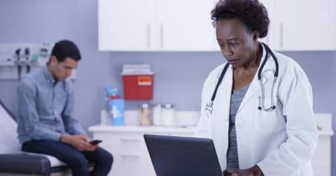 Portrait of doctor using portable computer to record notes of young male pati 스톡 사진