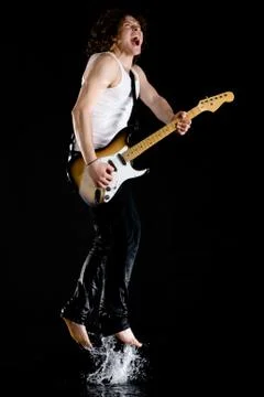Portrait of dynamic performer playing electrical guitar while jumping above wate Stock Photos