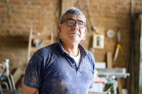 Portrait of an elderly carpenter posing and his workshop in the background. Stock Photos