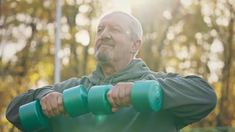 Portrait of an elderly energetic pensioner doing exercises with dumbbells in the Stock Footage 255714941