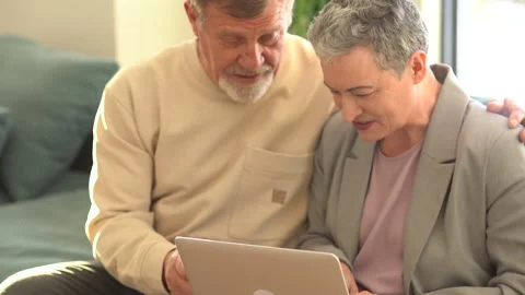 Portrait of an elderly gray-haired couple sitting on a sofa with a laptop on Stock Footage 169922527