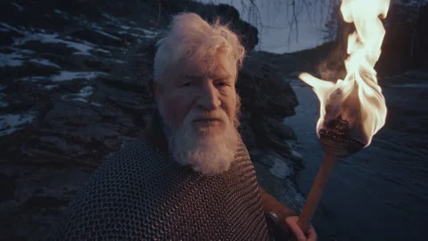 Portrait of Elderly Guard in Chainmail Holding Torch on Riverbank at Dusk Stock Footage 295535553