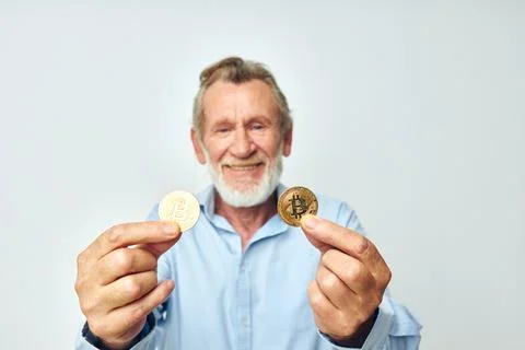Portrait elderly man in a blue shirt bitcoins on the face light background Stock Photos