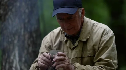 Portrait of an elderly man in a cap. he is sitting with a cup in the forest and Stock Footage 163666141