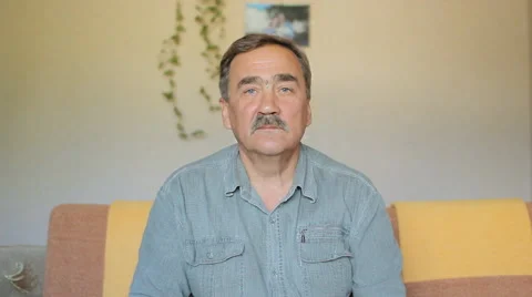 Portrait of elderly man with a mustache looking at camera at home on sofa Stock Footage 65374716