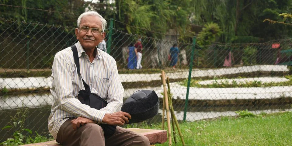 Portrait of elderly man sitting alone on bench at a Park in Shillong Stock Photos