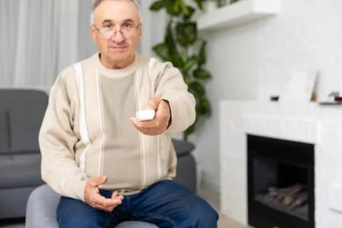 Portrait of elderly man using remote control while sitting on couch at nursing Stock Photos