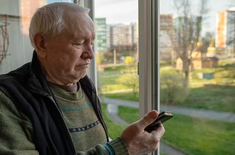 Portrait of an elderly man using a smartphone. Elderly man near the window .. Stock Photos