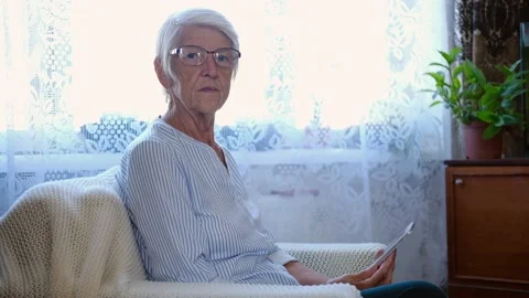 Portrait elderly woman holds in hands digital tablet reading ebook sit on sofa Stock Footage 178943553