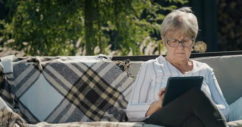 Portrait of an elderly woman using a tablet. Sitting in a garden swing in the Stock Footage 250857668