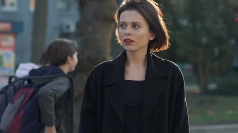 Portrait of elegant lady corrects her hairstyle from wind among sunny street Video stock 124731744