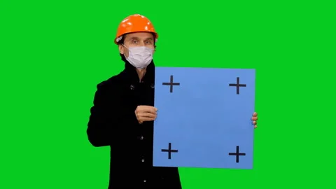 Portrait of an engineer in hard hat and mask holding blank board on green screen Видео 130794855
