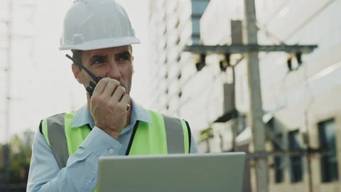 Portrait of engineer talking via radio set holding laptop standing against Stock Footage 300829929